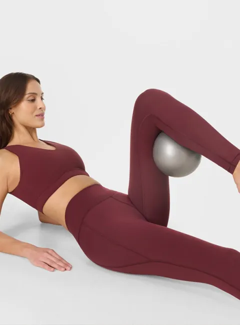 Vrouw doet workout op de grond in bordeauxrode 7/8 legging.