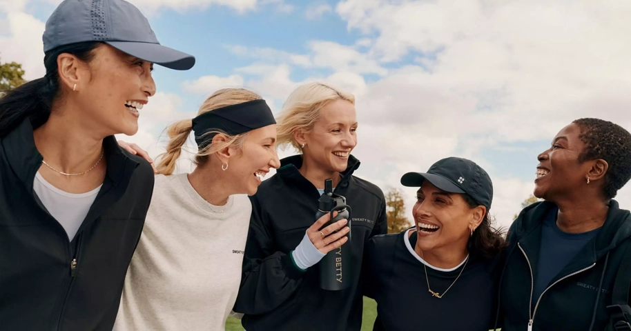 Vijf vrouwen in Sweaty Betty sportkleding lachen buiten.