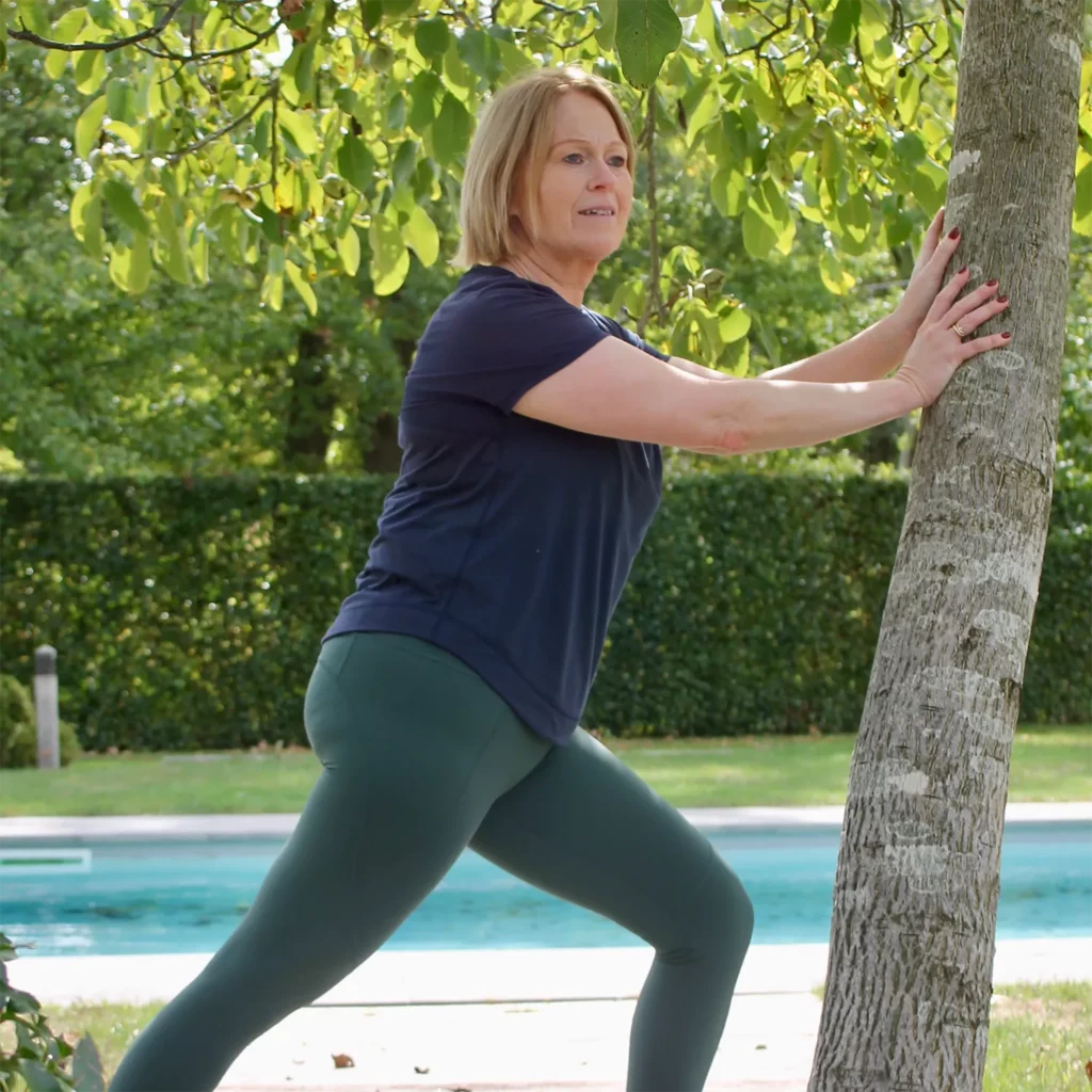 Vrouw strecht tegen een boom, in sportkleding van Sweaty Betty.