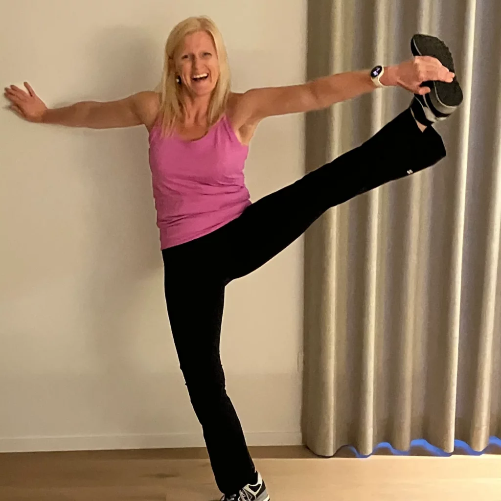 Vrouw in roze top doet een hoge beenoefening, in Sweaty Betty sportoutfit.